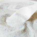 A person cleans a coffee stain from a fabric car seat with a spray bottle and cloth.