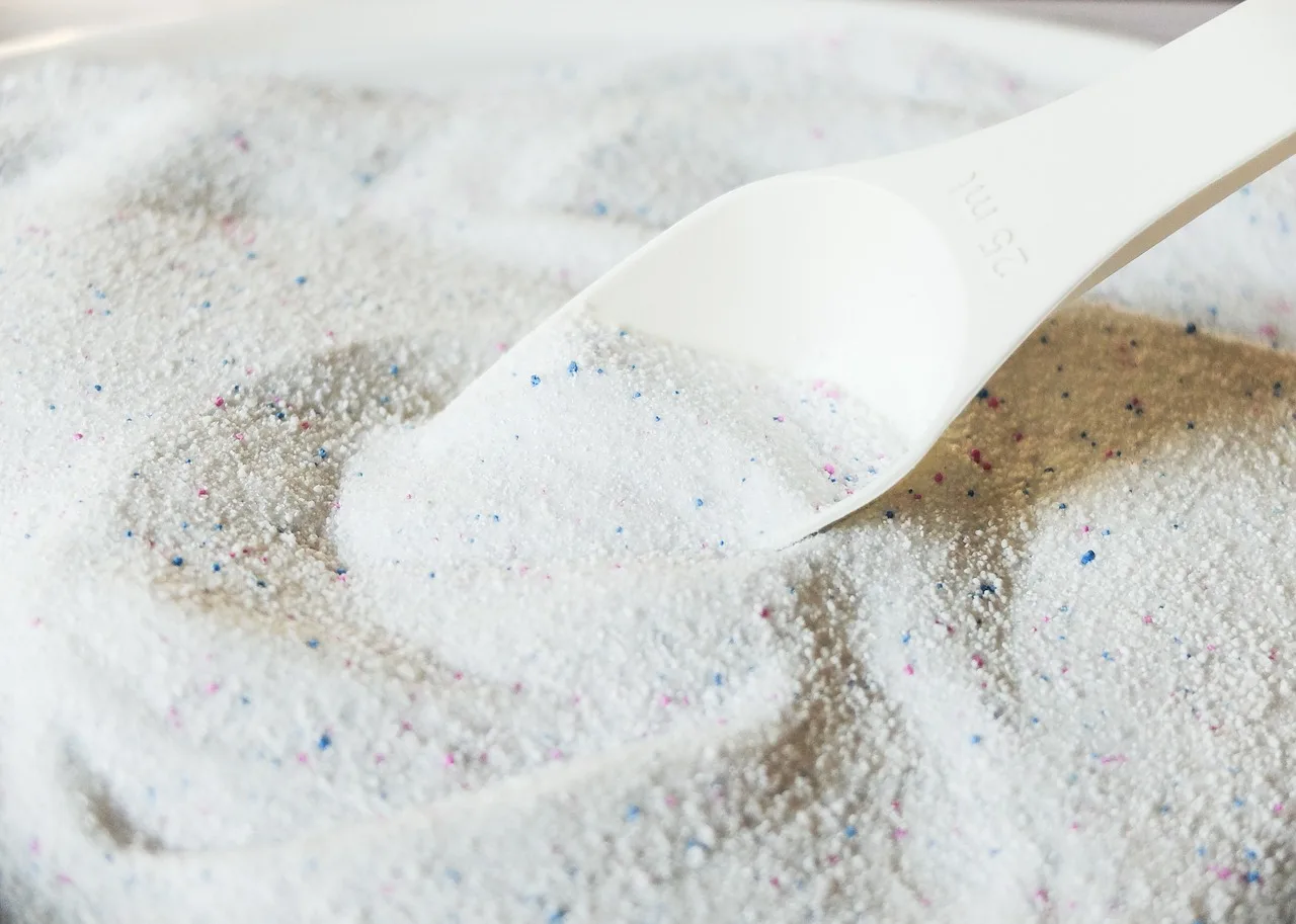 A person cleans a coffee stain from a fabric car seat with a spray bottle and cloth.