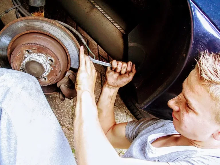 A car wheel with light gray brake dust and a mechanic pointing near the rim