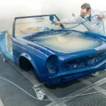 Detailer applying ceramic spray on a black car hood with glossy reflections in natural light