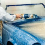 Detailer applying ceramic spray to a car hood and wiping it with a microfiber towel in daylight.