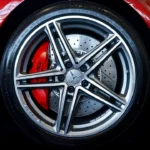 A detailer inspects dirty alloy wheels covered in brake dust beside a car with cleaning tools nearby.