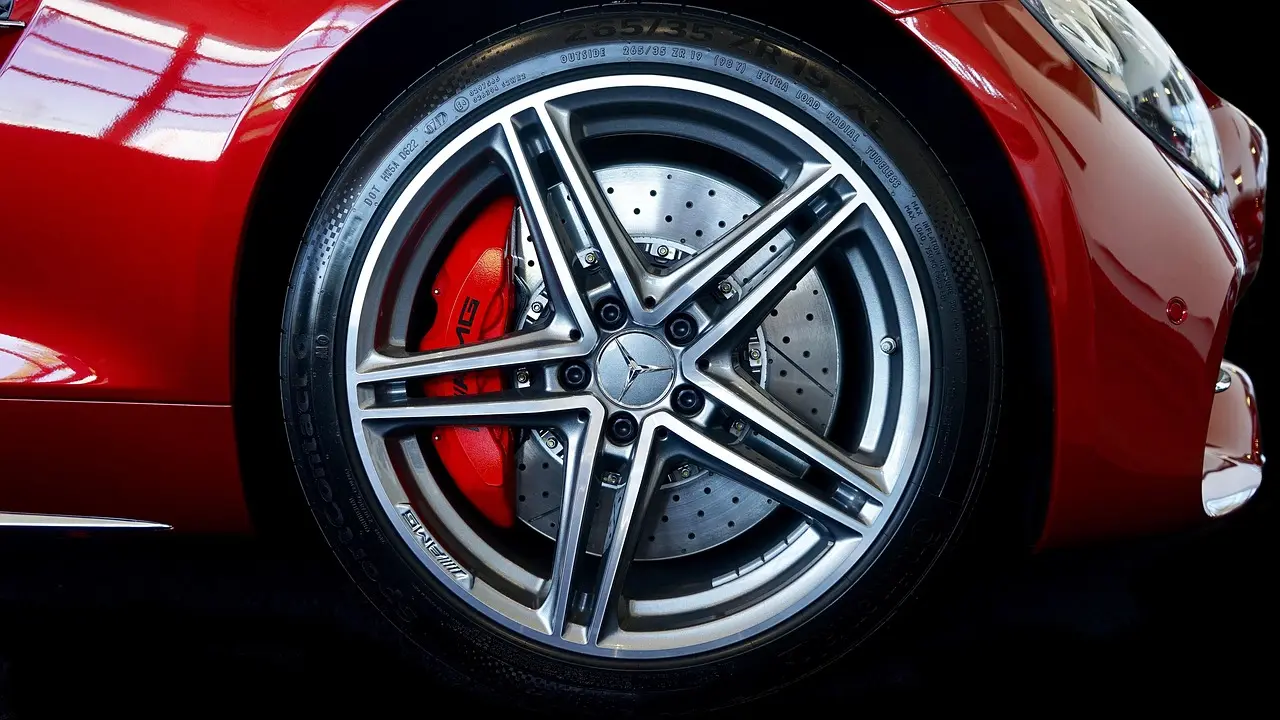 A detailer inspects dirty alloy wheels covered in brake dust beside a car with cleaning tools nearby.