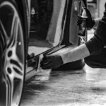 Person hand washing a dark car with a microfiber mitt and buckets in natural daylight