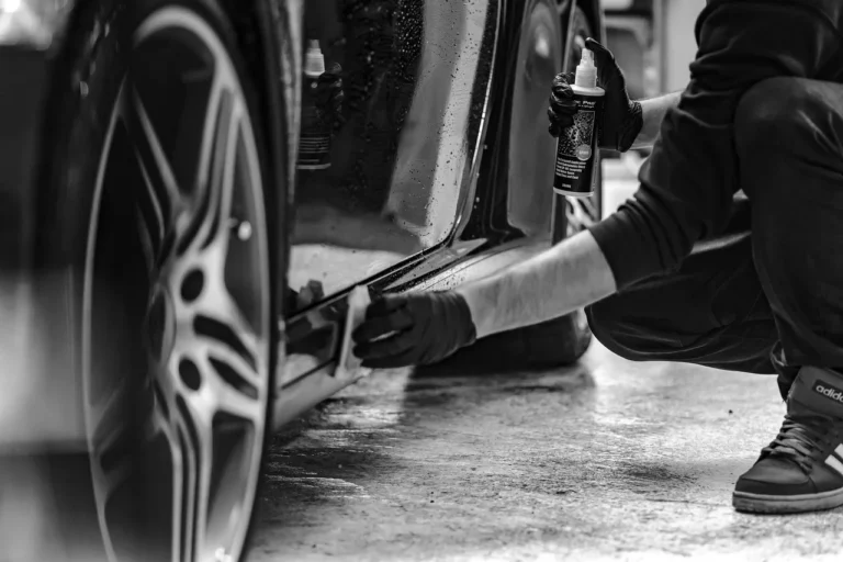 Person hand washing a dark car with a microfiber mitt and buckets in natural daylight