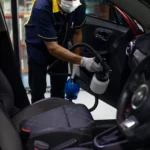 Person cleaning a car interior with vacuum and cloth to remove cigarette smoke smell from a car