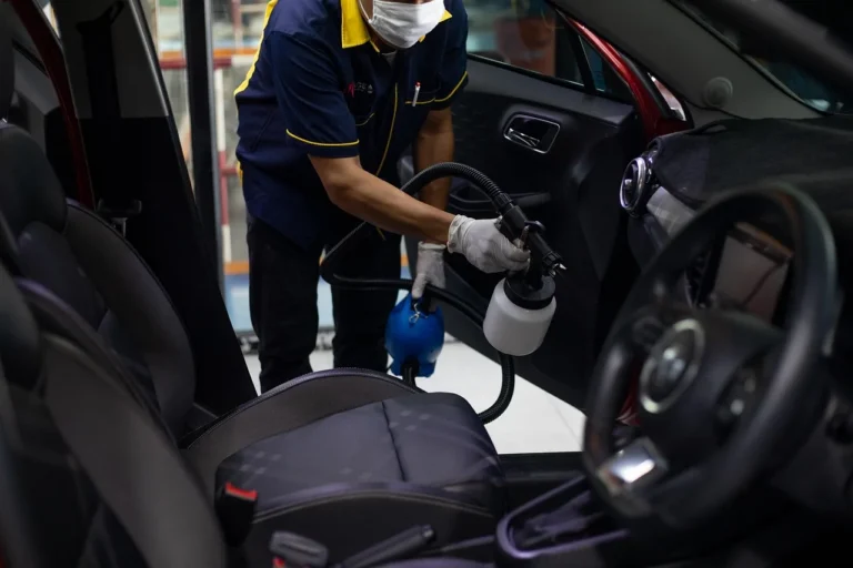 Person cleaning a car interior with vacuum and cloth to remove cigarette smoke smell from a car