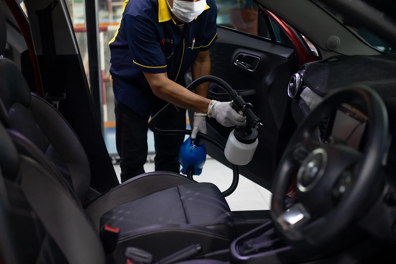 Person cleaning a car interior with vacuum and cloth to remove cigarette smoke smell from a car