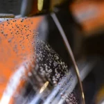 Car windshield with light water spots being inspected beside a spray bottle and microfiber cloth