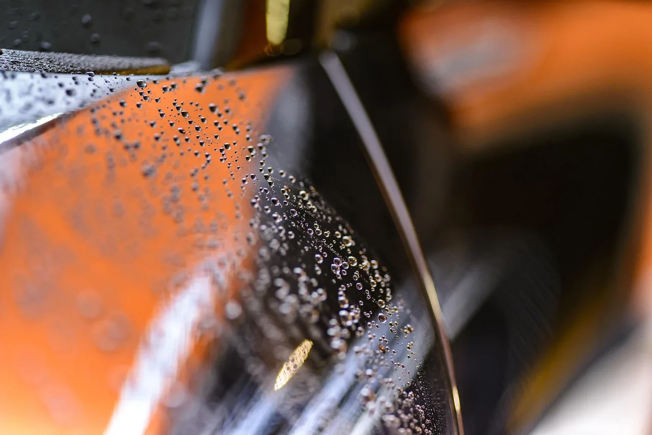 Car windshield with light water spots being inspected beside a spray bottle and microfiber cloth