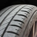 A daily driver sedan in a driveway with one freshly dressed tire in natural light