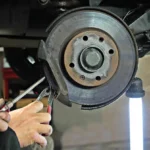 A car wheel with light gray brake dust on the rim and visible brake rotor in daylight