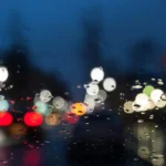 A person inspects water spots on a car windshield in natural daylight