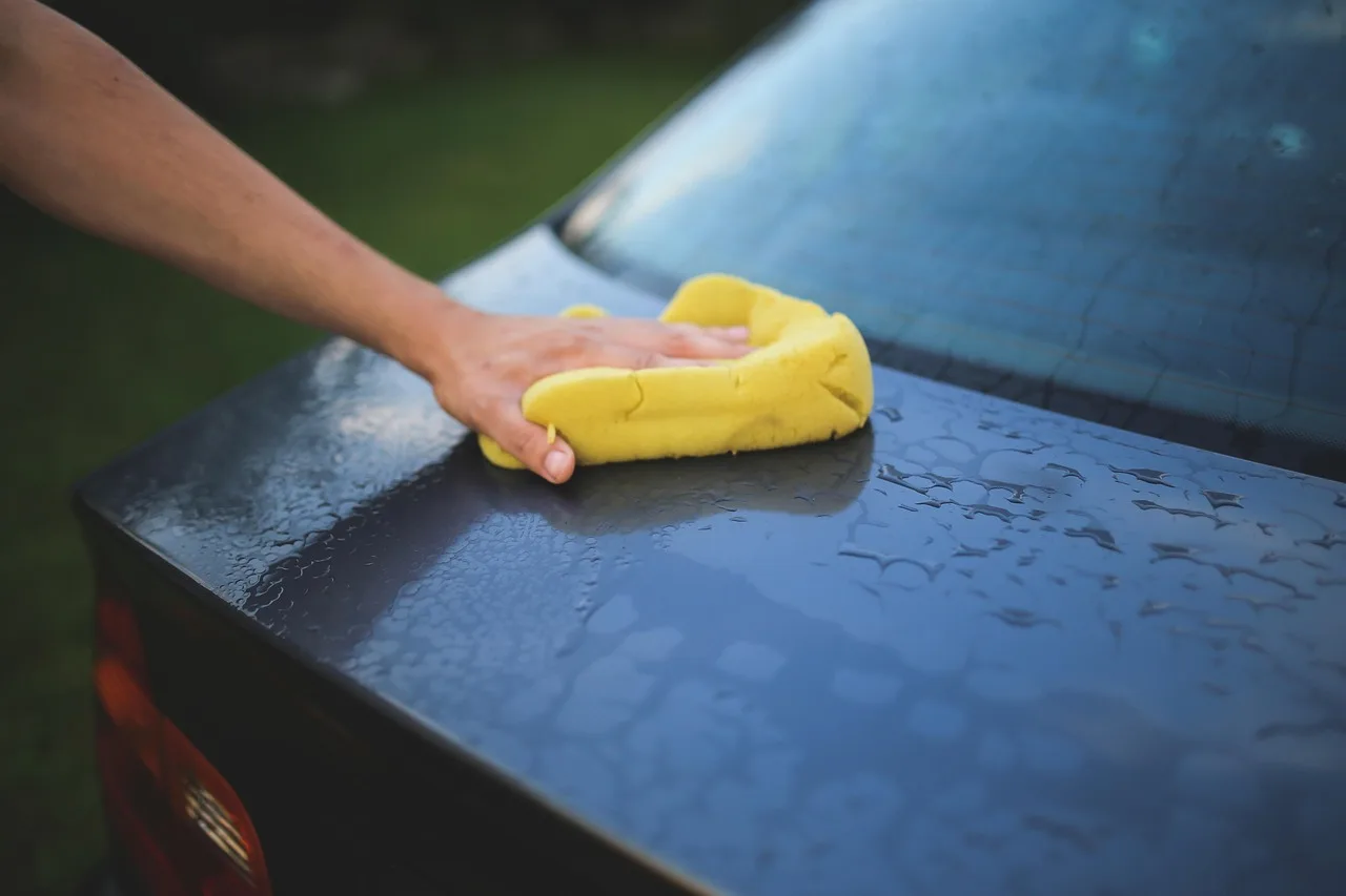 Person hand washing a car in a driveway with bucket, hose, and microfiber mitt