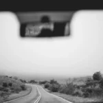 Driver inspecting a foggy windshield with a hazy interior film in soft morning light