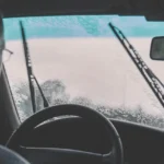 Driver inspects a dirty windshield inside an older sedan in natural morning light