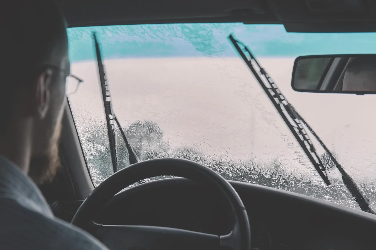 Driver inspects a dirty windshield inside an older sedan in natural morning light